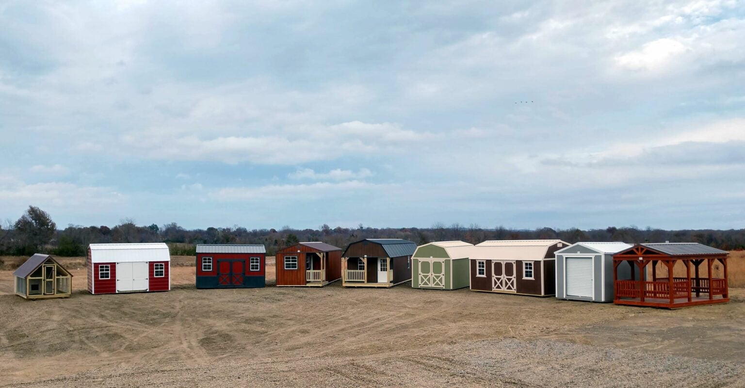 Nine Burnett buildings lined up on a sales lot, from a chicken coop and lofted barns to cabins, a garage and a gazebo