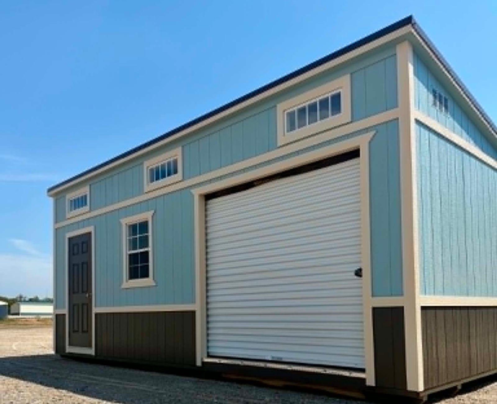 Side view of a light blue Burnett studio shed showing the roll-up door and transom window band
